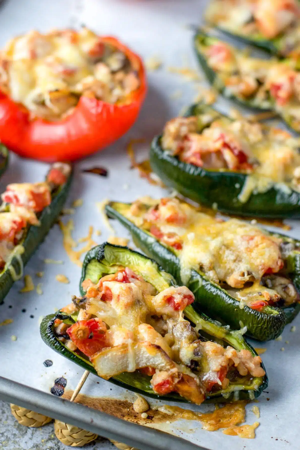 A parchment lined pan full of peppers stuffed with chicken and veggies