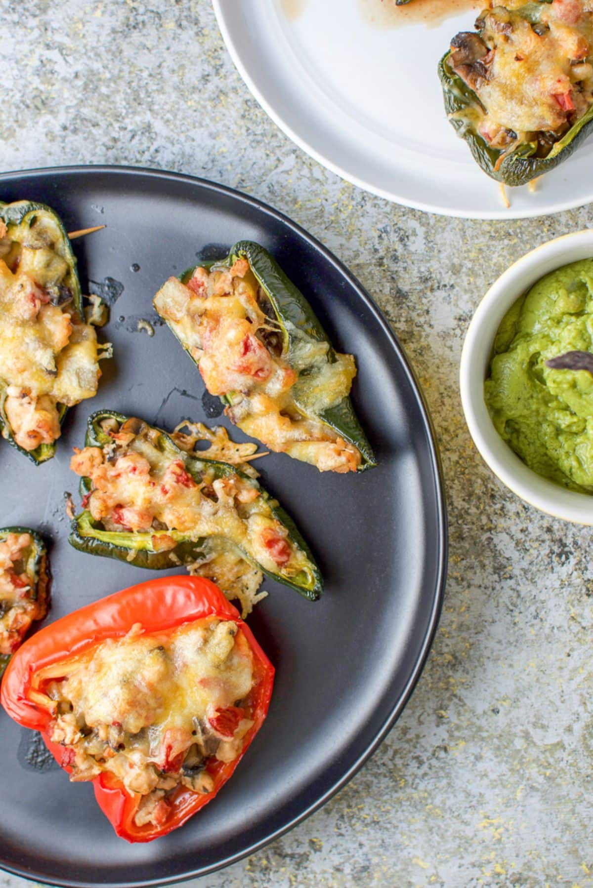 Overhead view of a black plate with stuffed peppers on it along with some guacamole