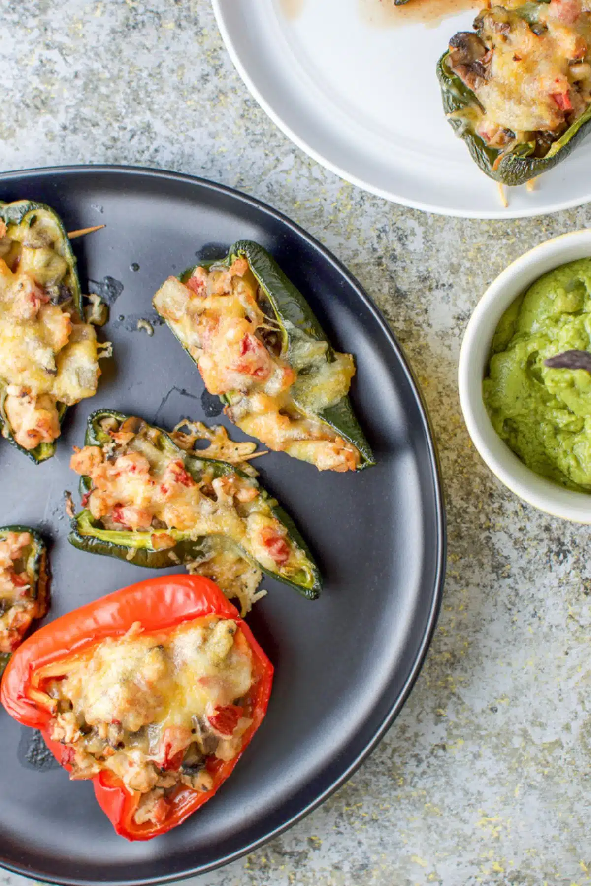 Overhead view of a black plate with stuffed peppers on it along with some guacamole