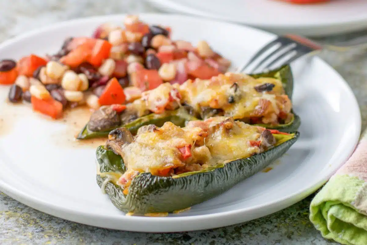 A white plate with two stuffed peppers with bean salad