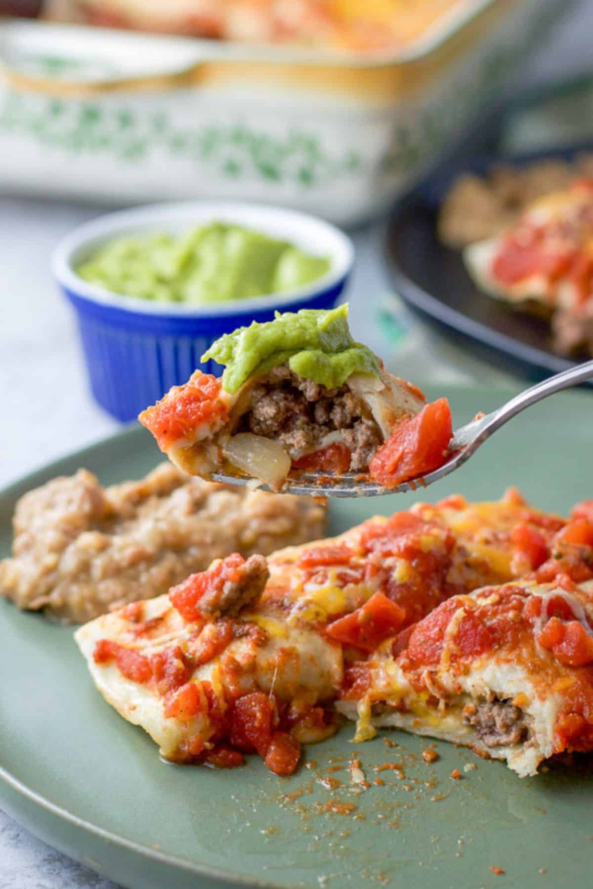 Forkful of a bite of beef enchiladas ready to be eaten.