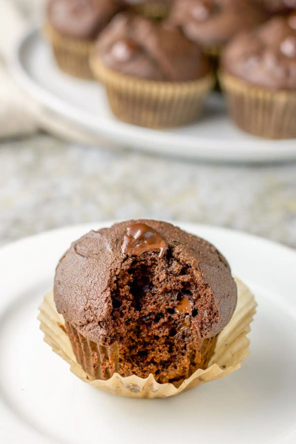 A small plate with a muffin on it with the baking cup loosened and a bite taken out of the gooey muffin