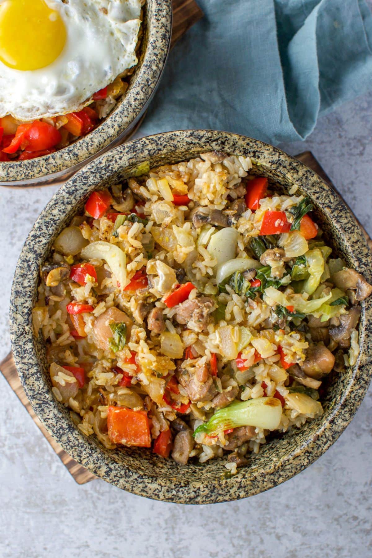 overhead view of two stone bowls filled with rice, veggies, and chopped chicken