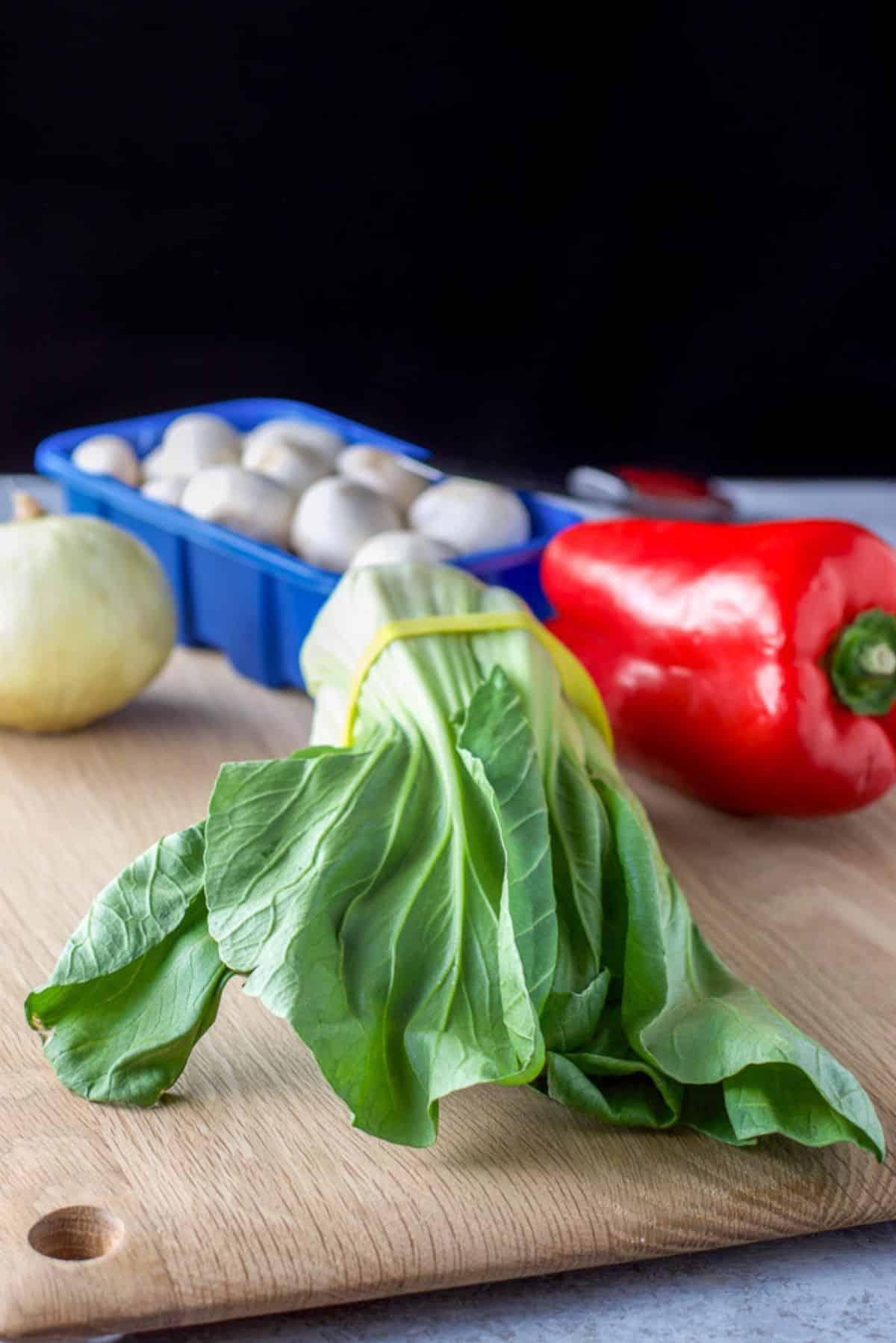 Bok choy, red bell pepper, mushrooms, snd onion on a wooden board
