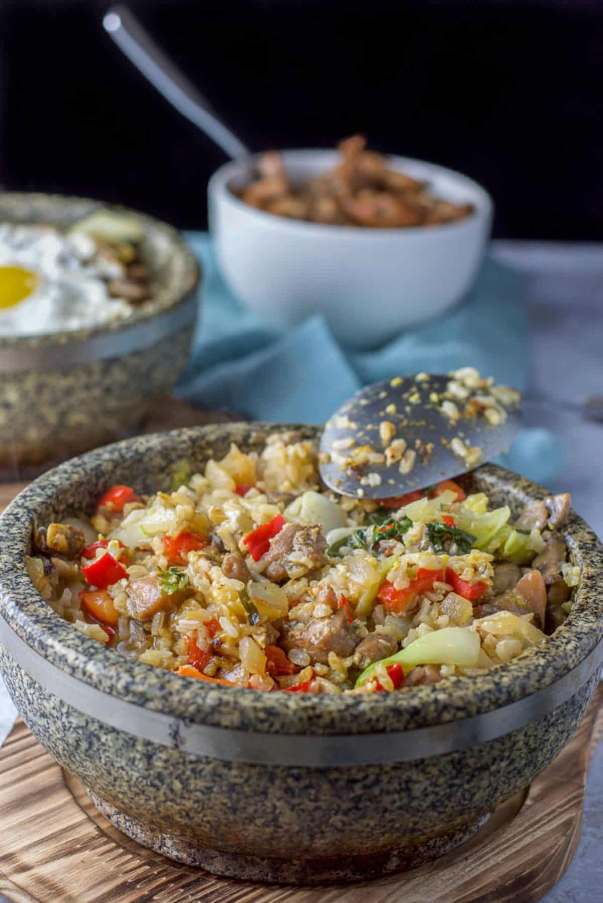 Two stone bowls with mixed rice, vegetables, egg, and chicken