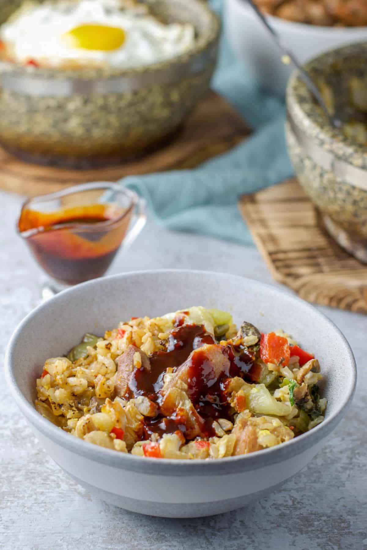 A grey bowl filled with the bibimbap with sauce on it, with the bowls in the back