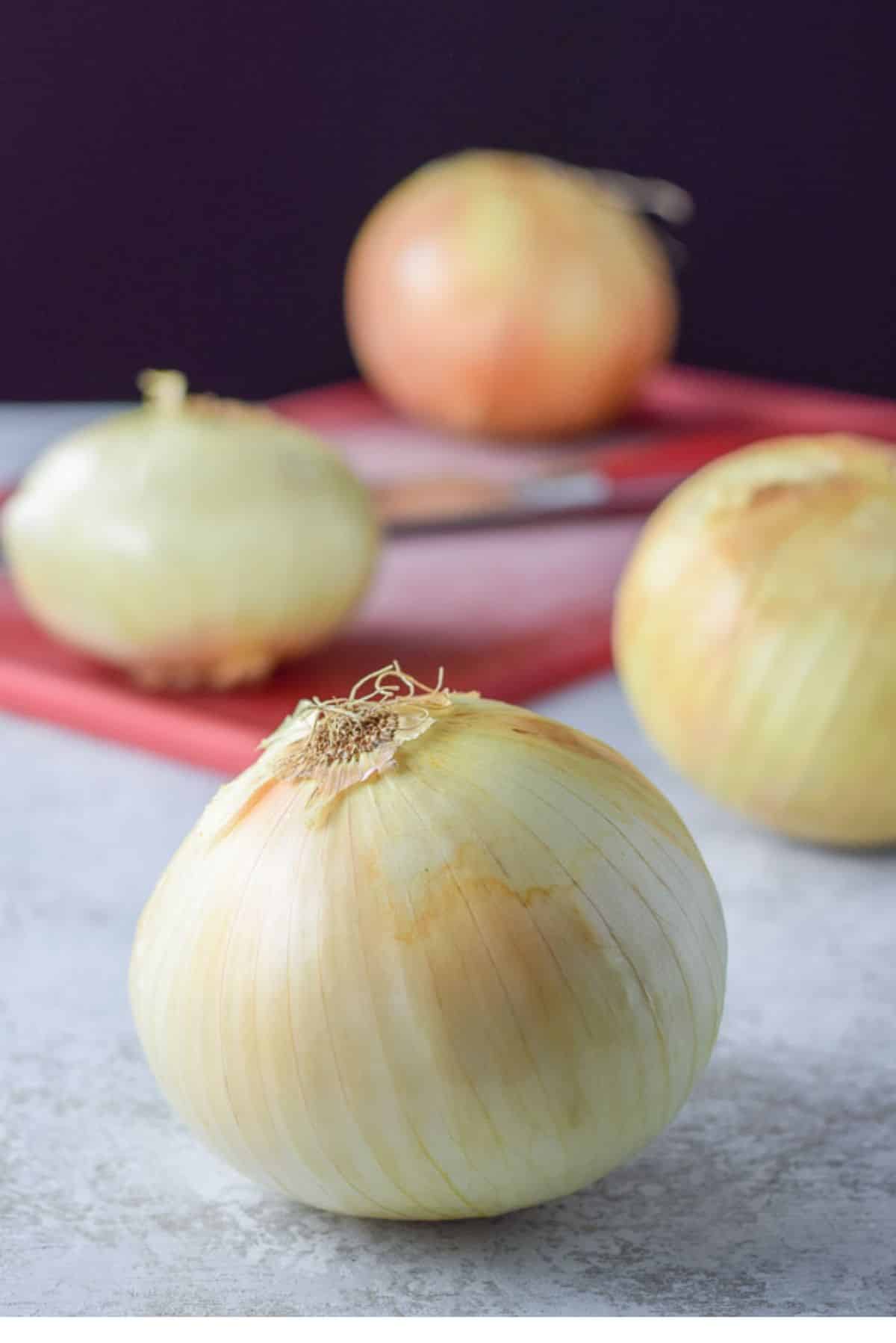 Onions on a board and a knife on the red cutting board