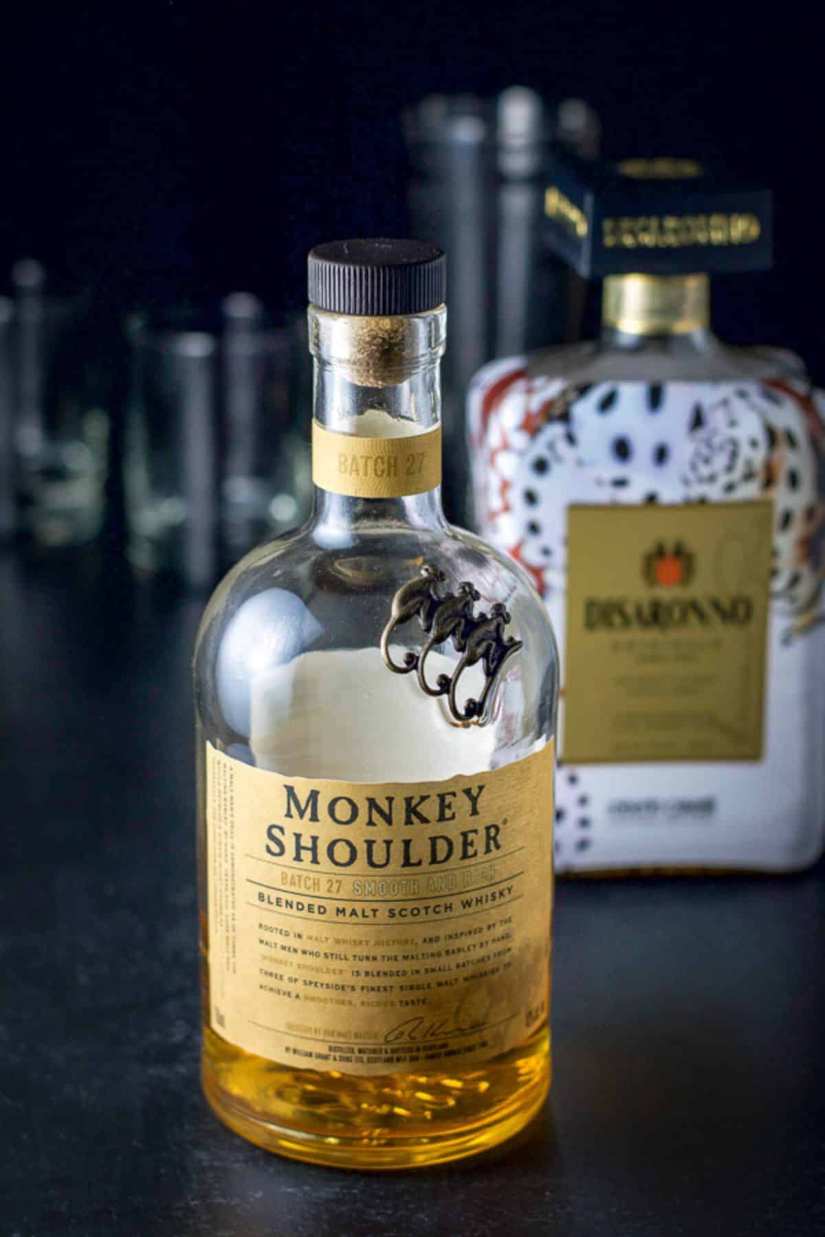 Scotch, almond liqueur in front of a cocktail shaker and 2 glasses