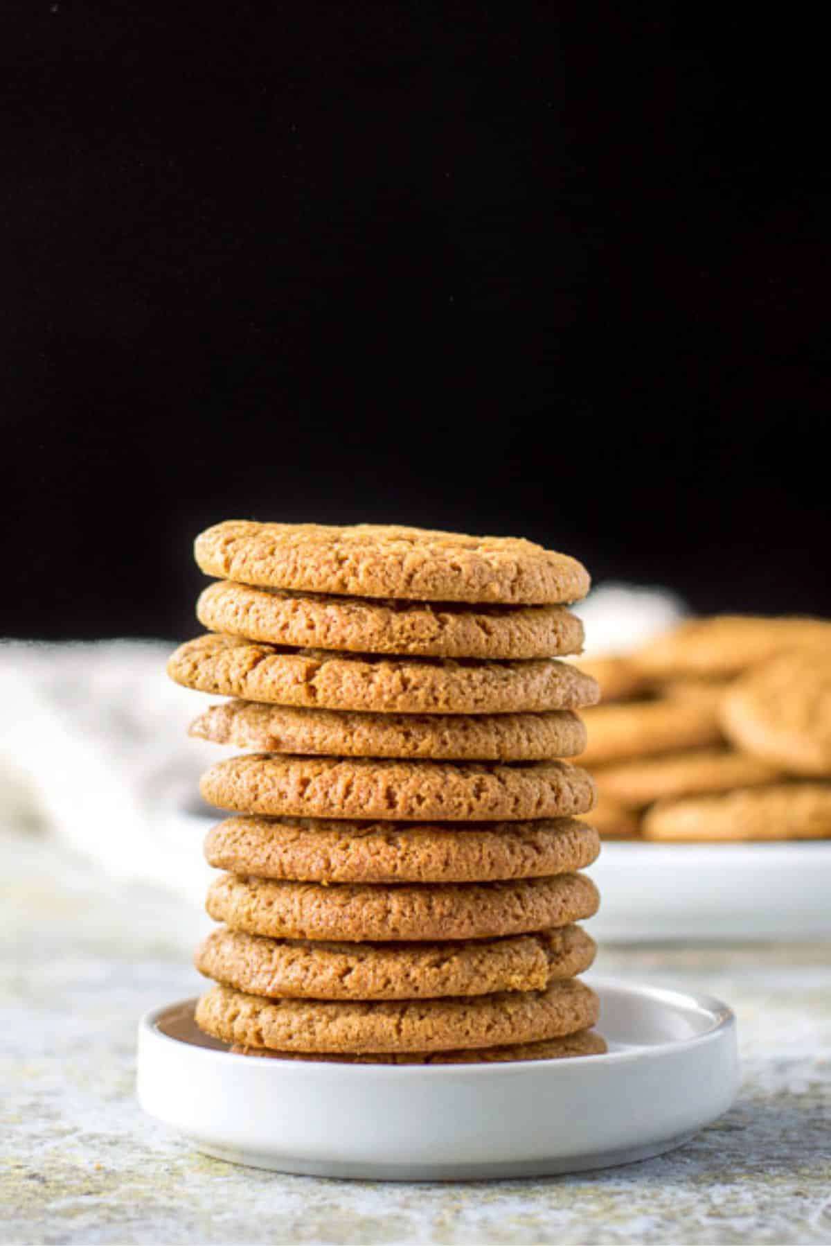 Tower of molasses cookies in a small white plate with more cookies in the background