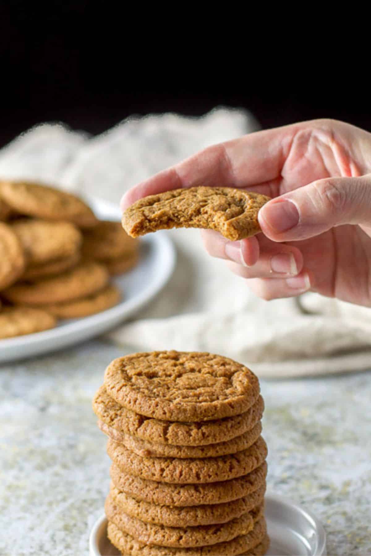 A hand holding a cookie with a bite taken out of it. There are more cookies in the background