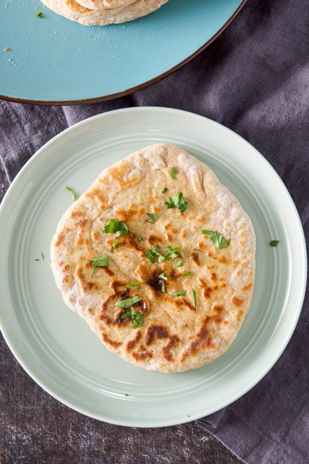 Overhead view of a piece of naan with butter and cilantro on it