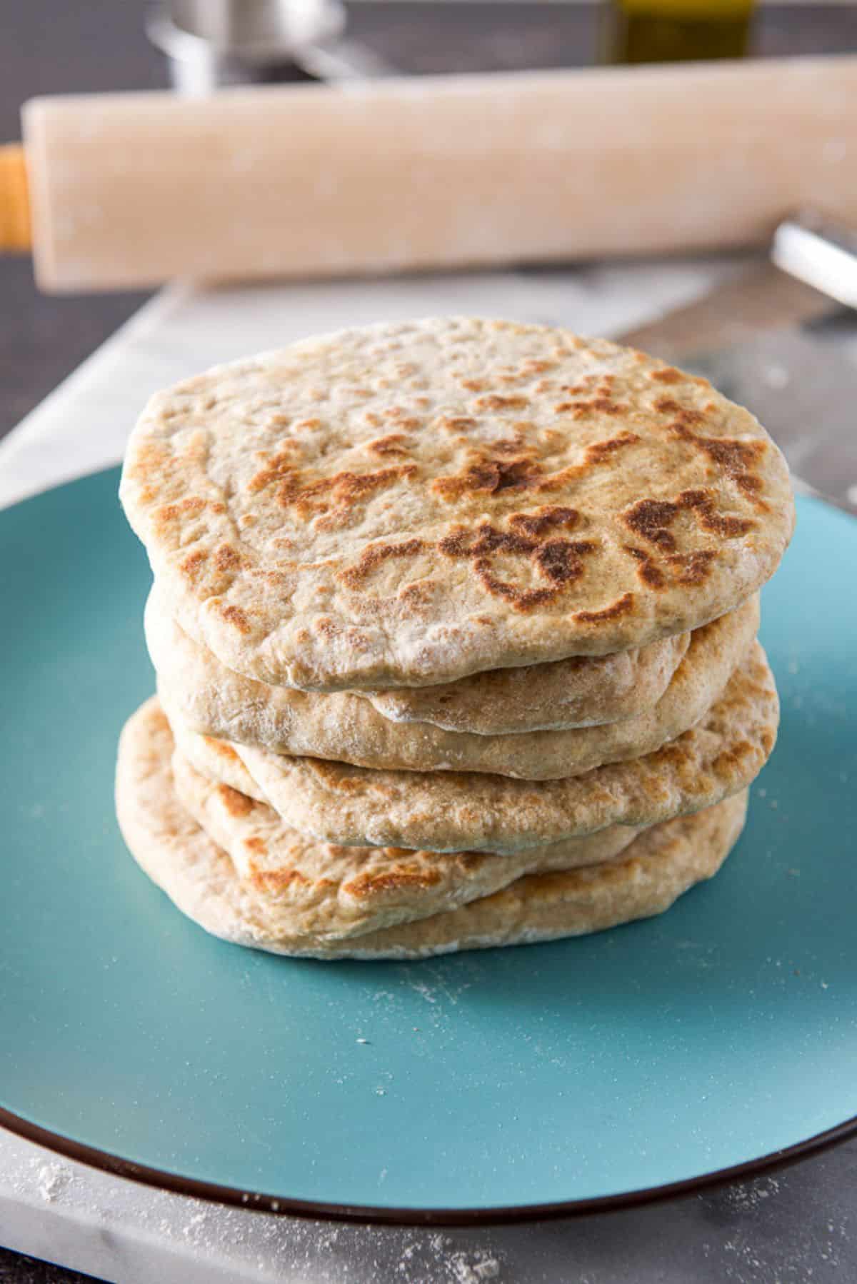 A blue green plate with six pieces of naan bread on it with a rolling pin in the back