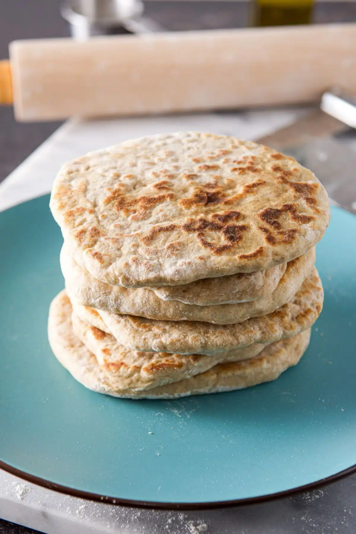 A blue green plate with six pieces of naan bread on it with a rolling pin in the back