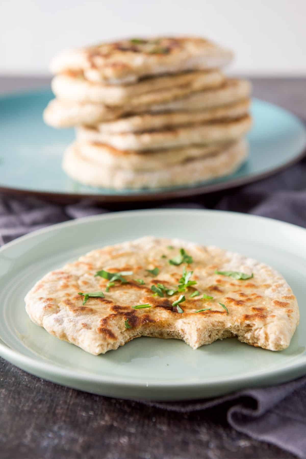 A green plate with a piece of naan on it with two bites out of it. There is a stack of naan in the back