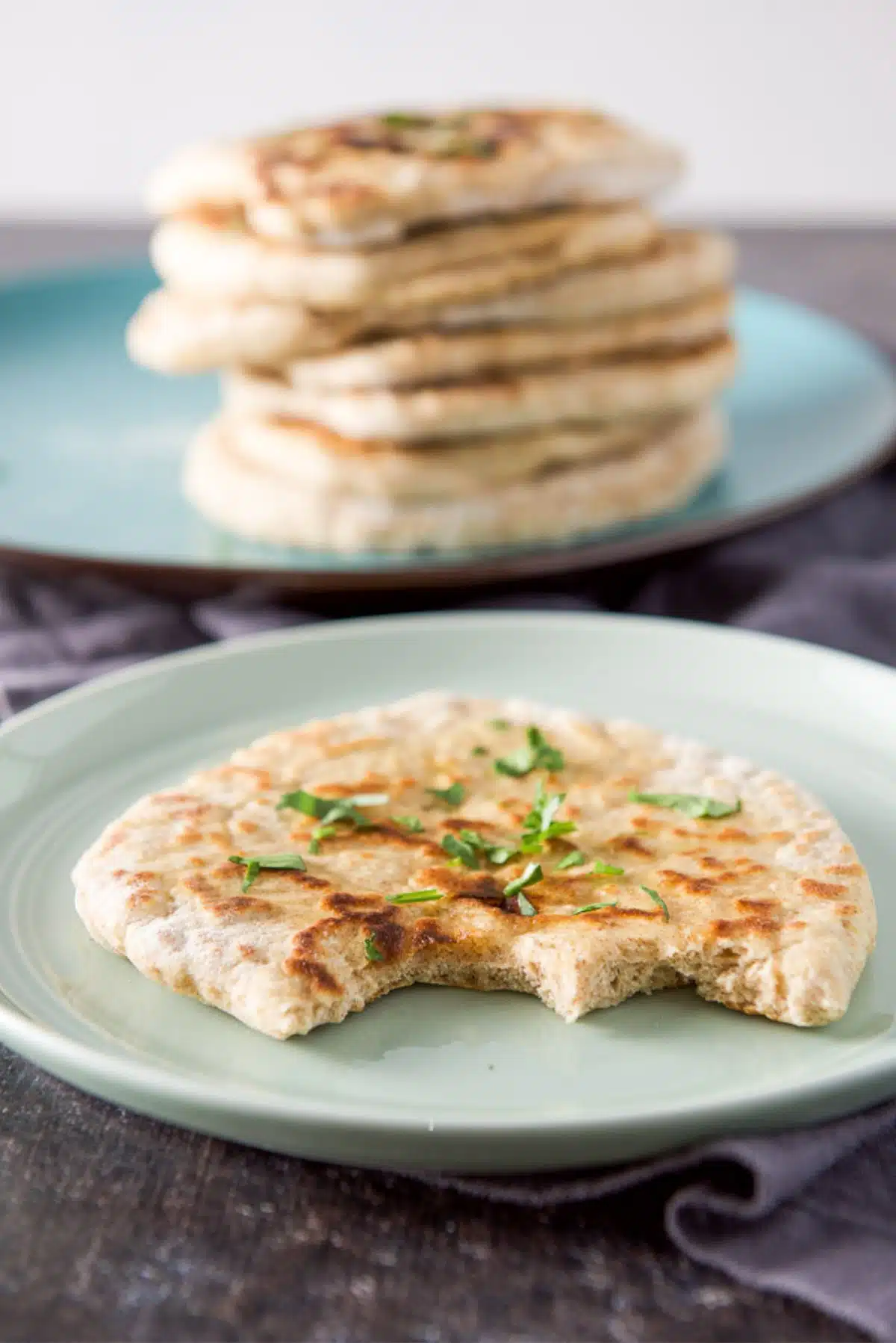 A green plate with a piece of naan on it with two bites out of it. There is a stack of naan in the back