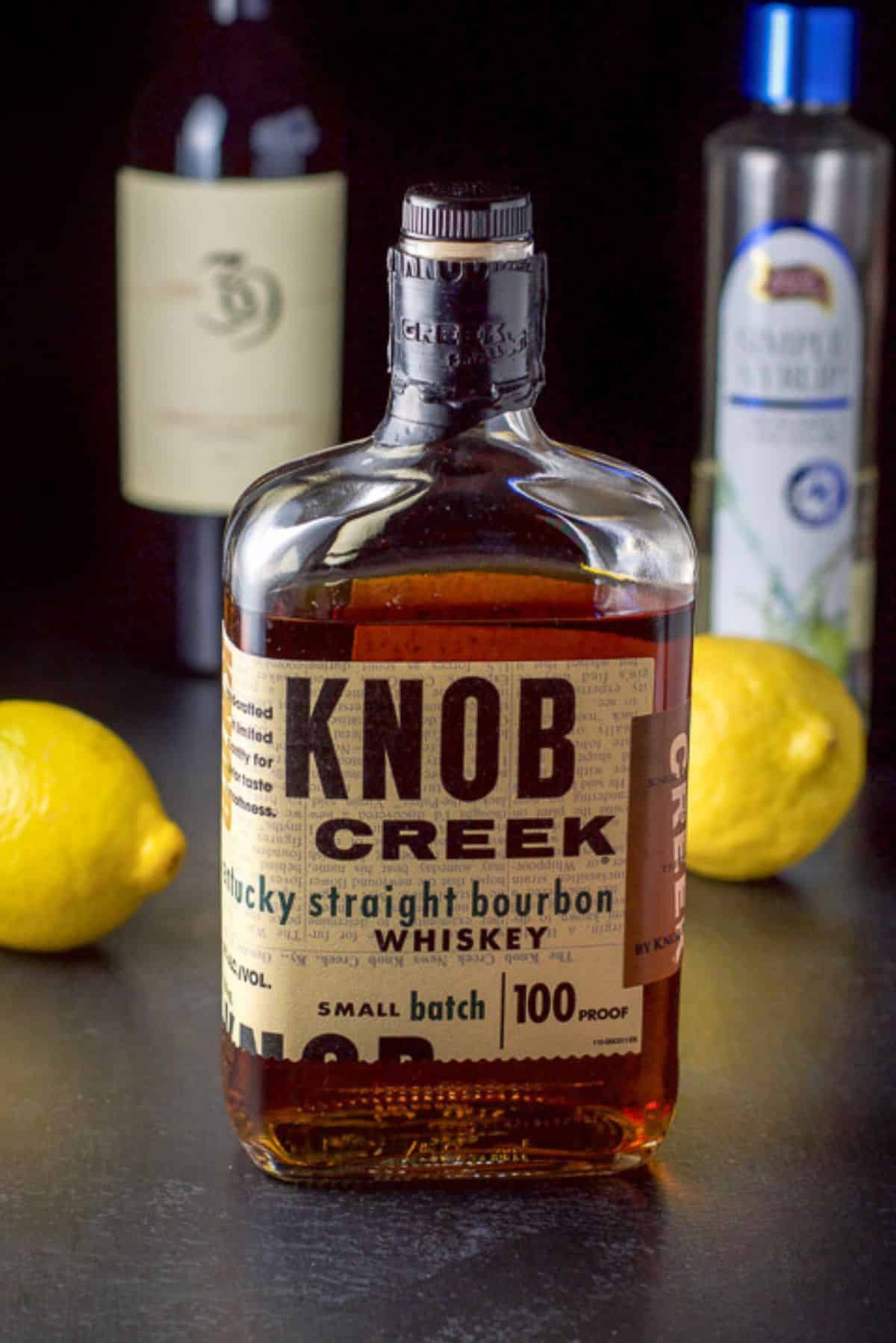 Bourbon, lemon, simple syrup, and wine on a black table