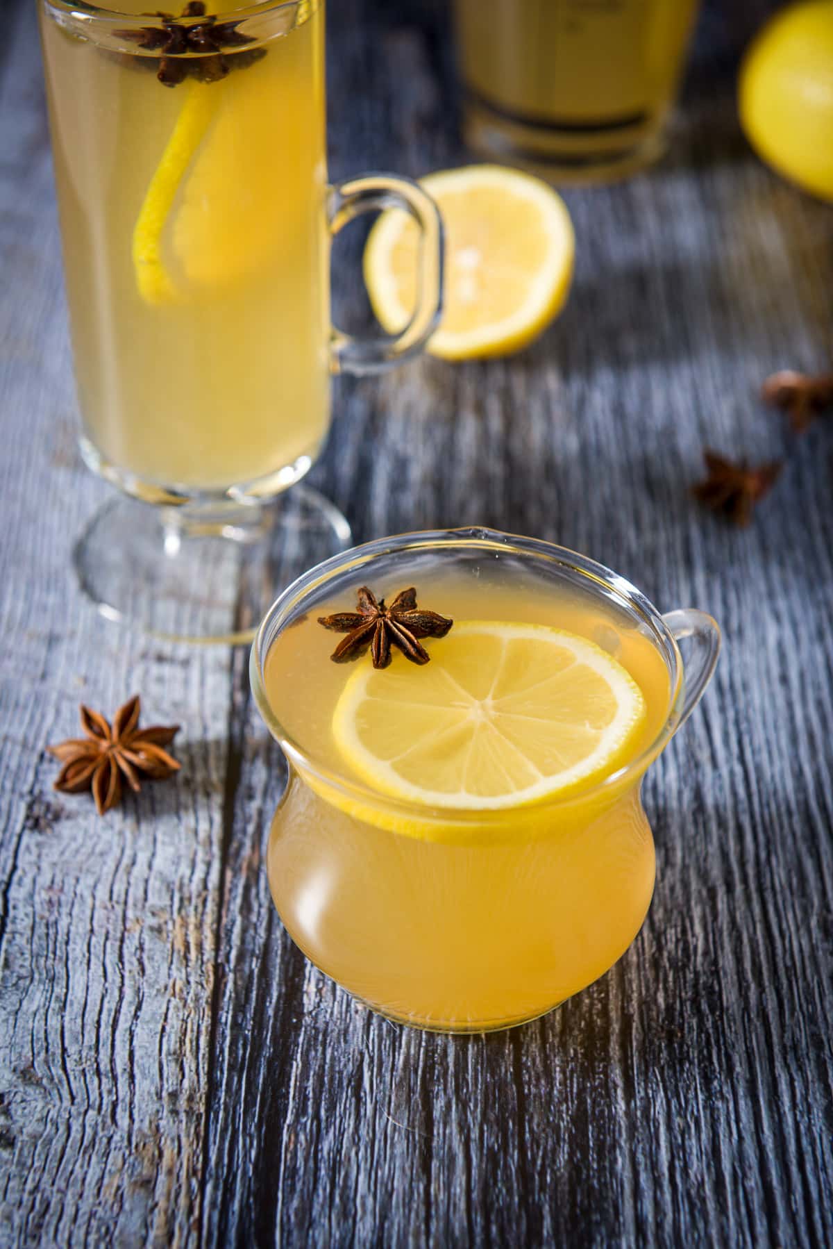 Star anise floating in a lemon drink with another glass in the back with lemons and more star anise