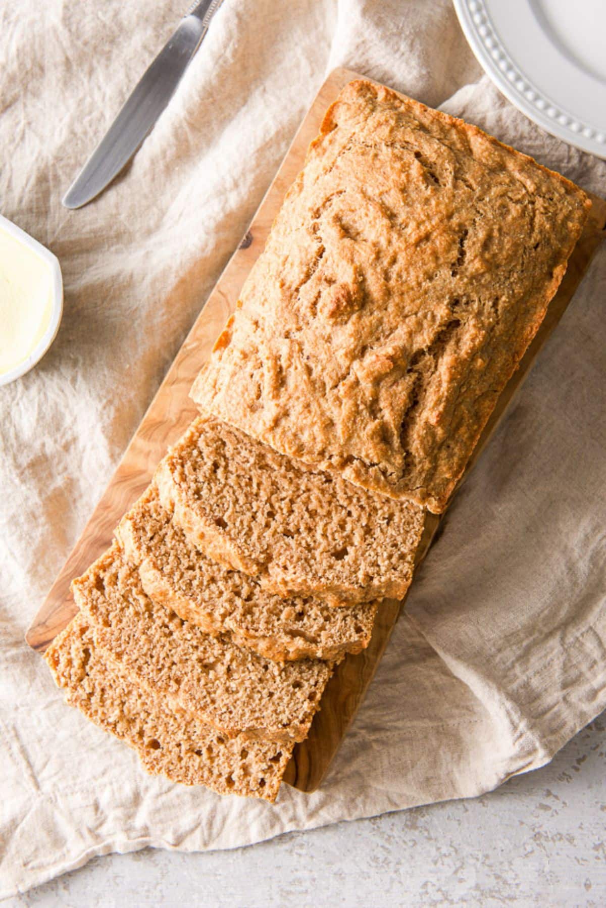 Overhead view of the brown quick bread on a wooden board, and butter, a knife and a plate on a napkin