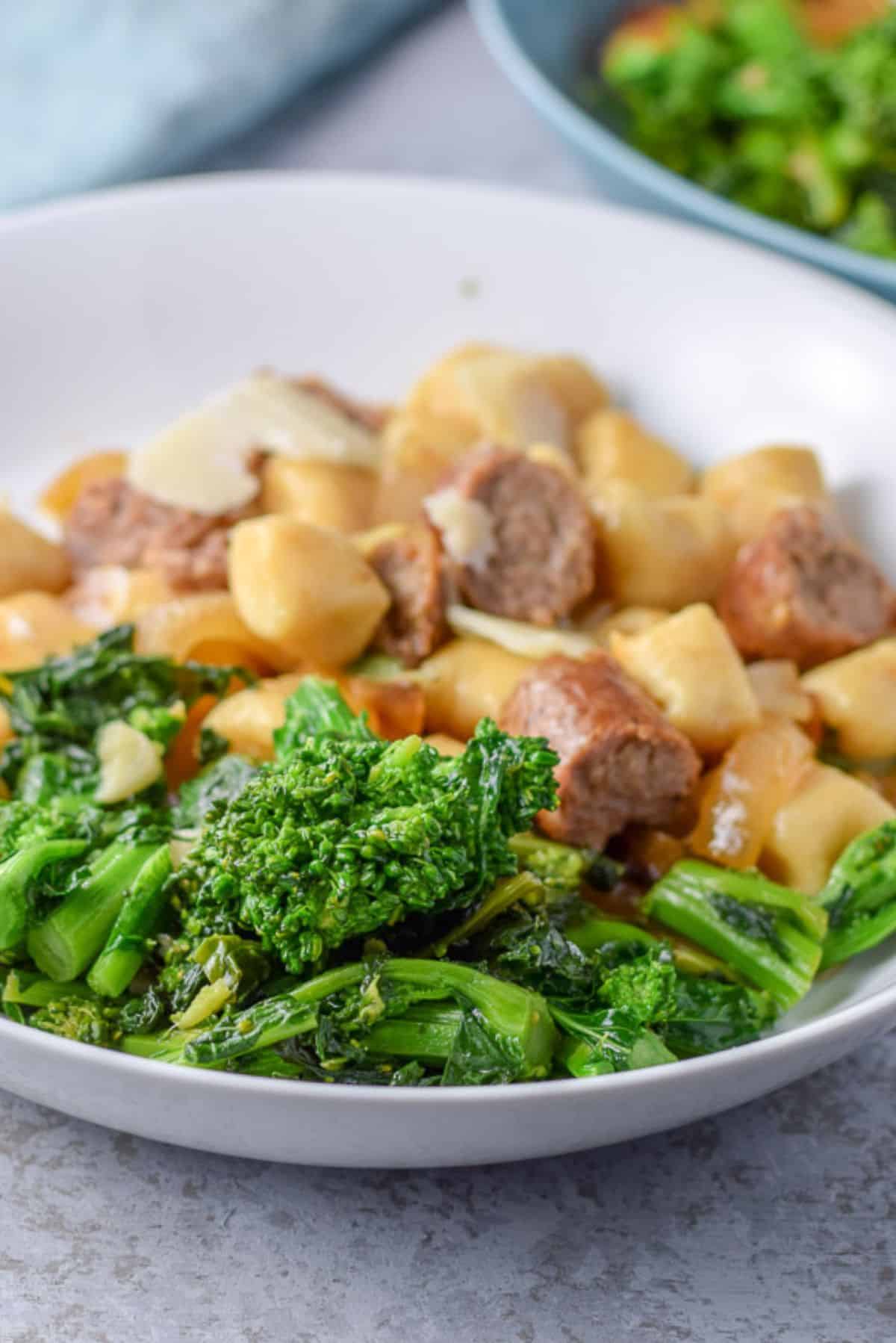 Close view of a white dish with gnocchi and sausage with broccoli rabe in the front