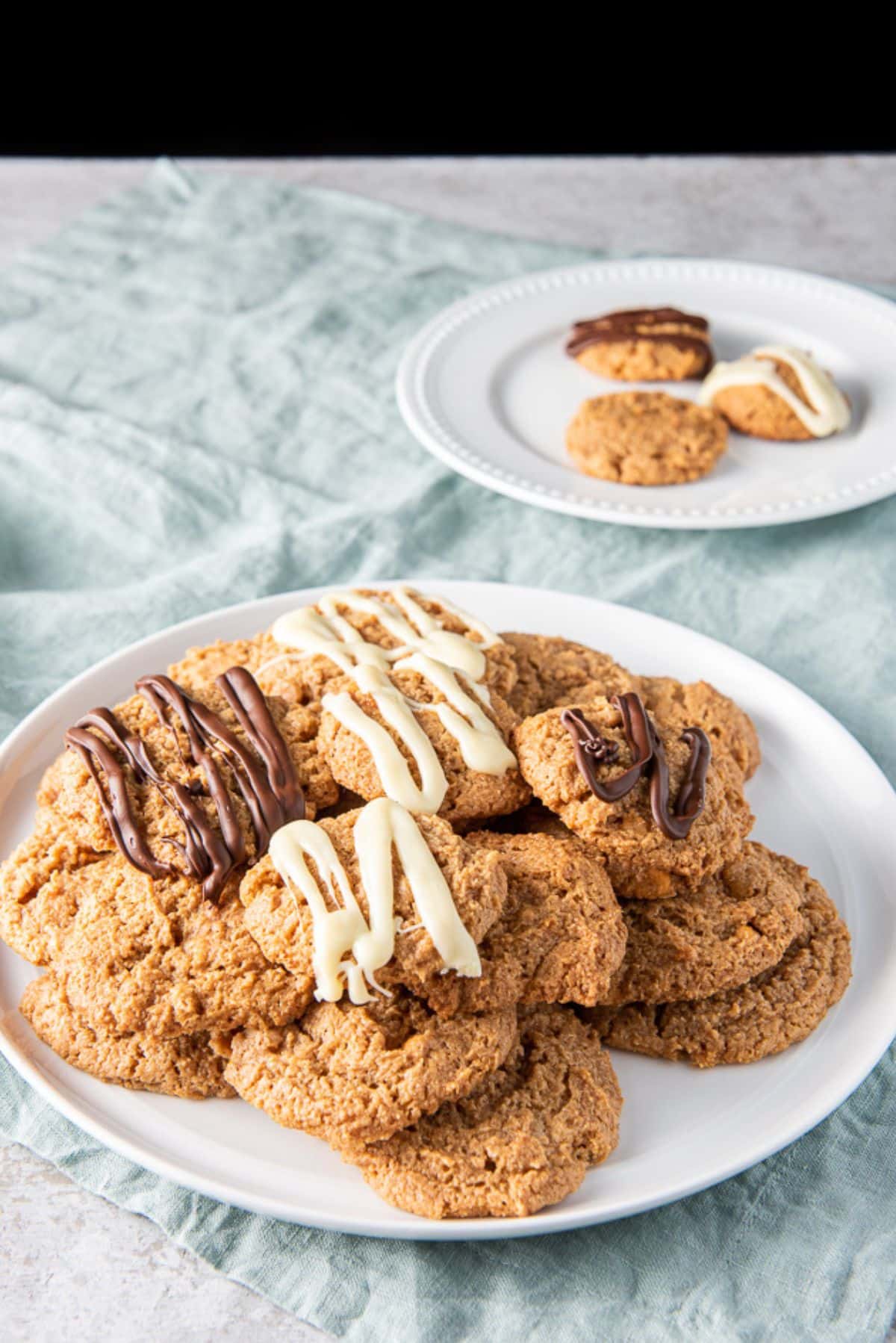 A pile of butterscotch cookies on a plate white plate with a few cookies on another plate behind it