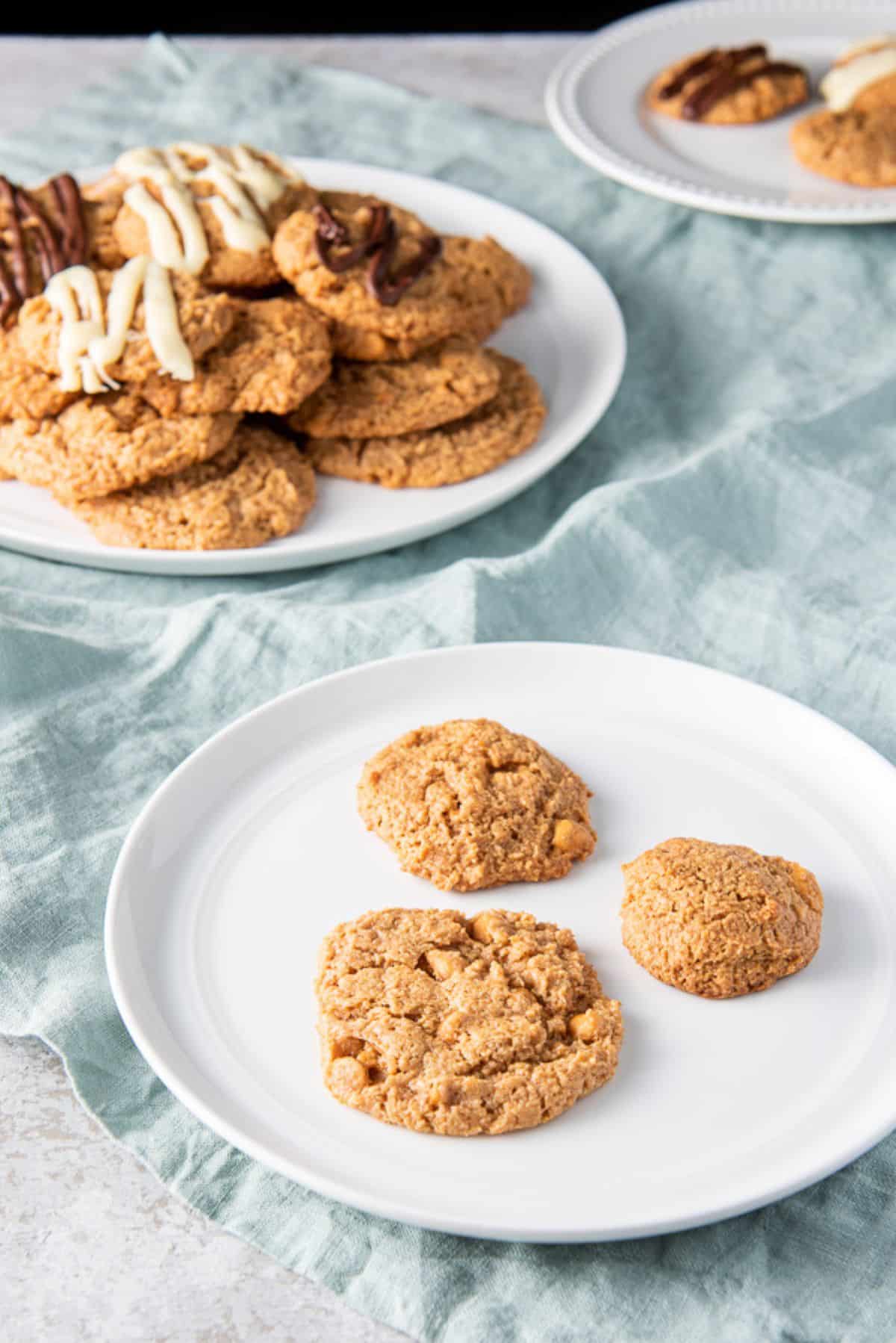 Three different sized cookies on a white plate with the big plate of cookies behind it
