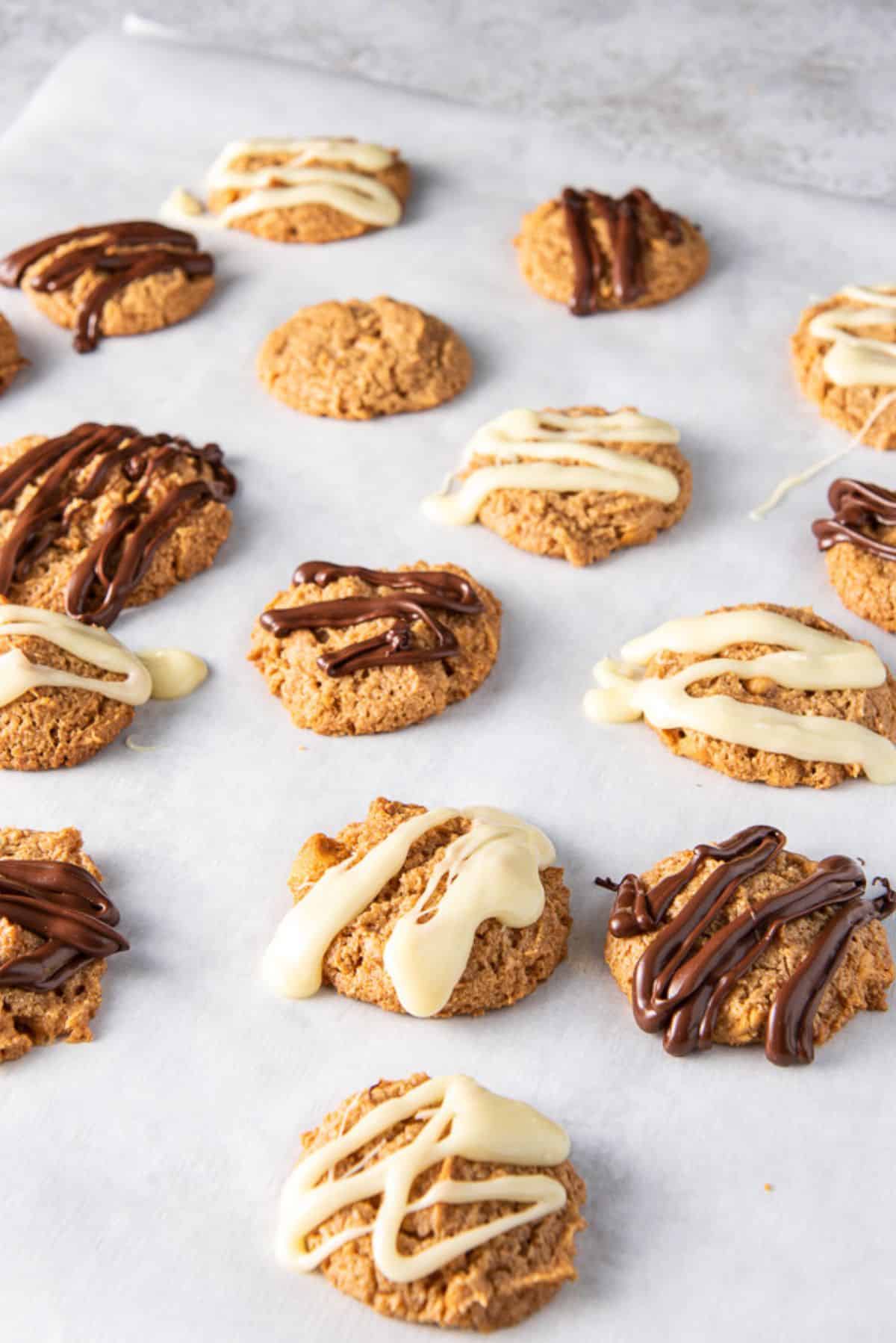 A large piece of parchment paper with butterscotch cookies and chocolate drizzle on them