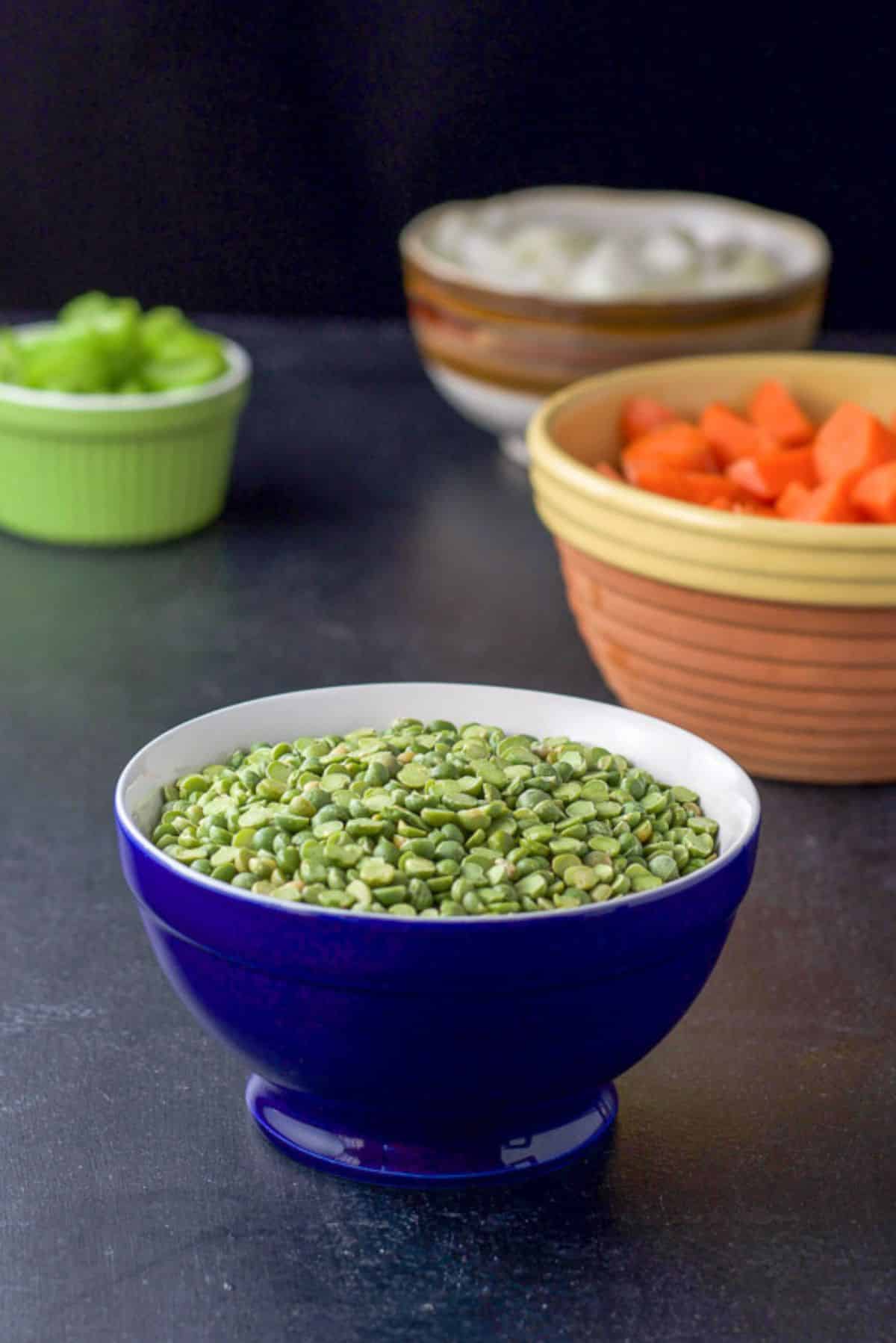 Split peas, carrots, onions, and celery in bowls on a black board