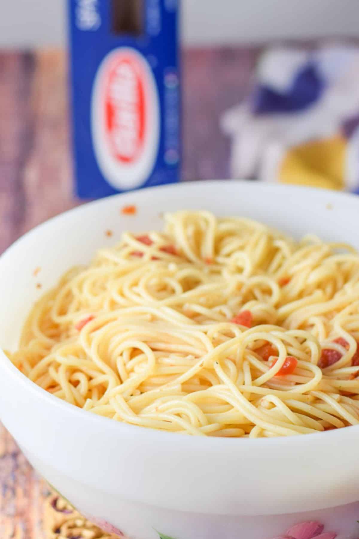 A white bowl of pasta with some chunky tomato sauce on it so the spaghetti is a pinkish color
