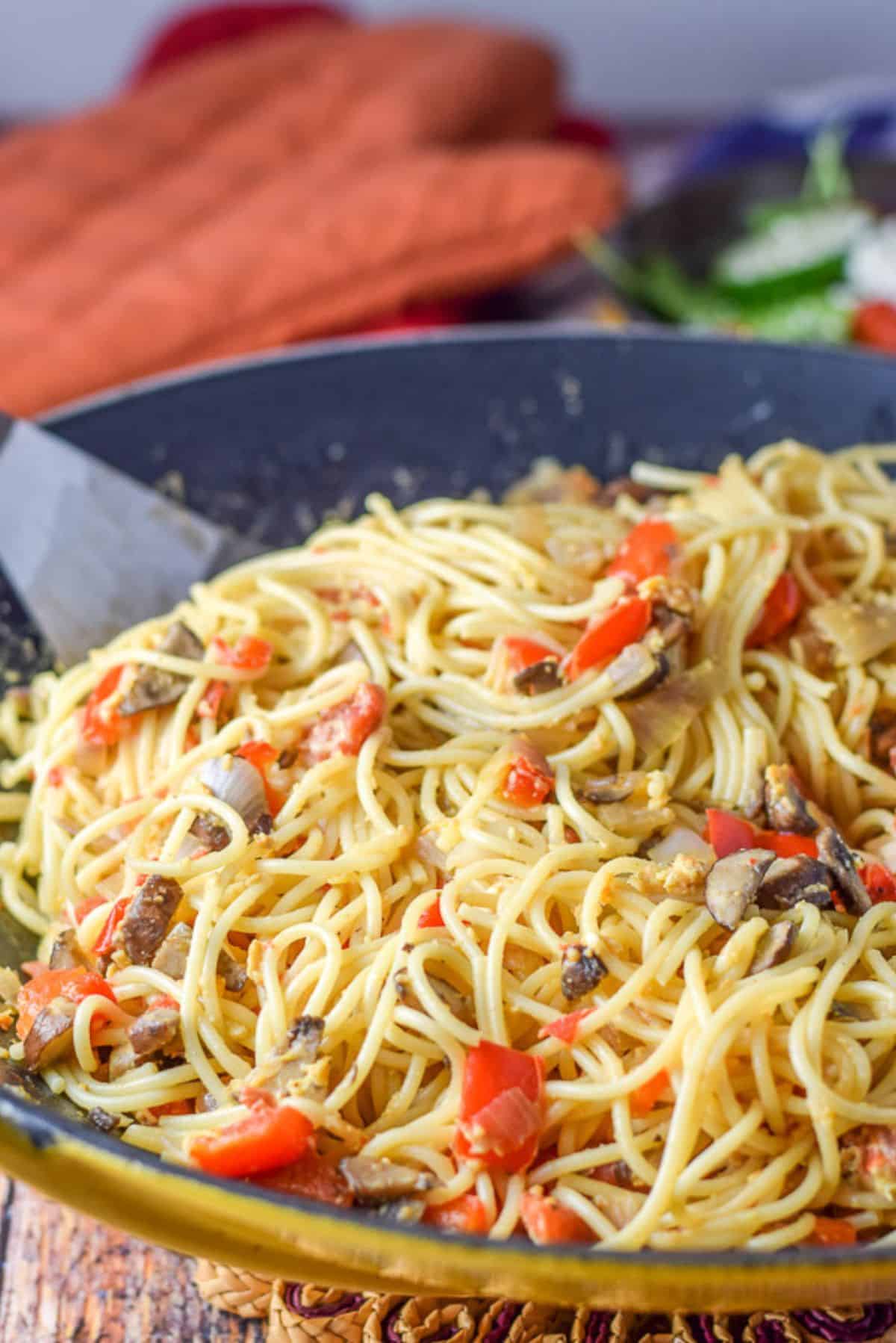 A wok filled with the spaghetti dish with veggies in it