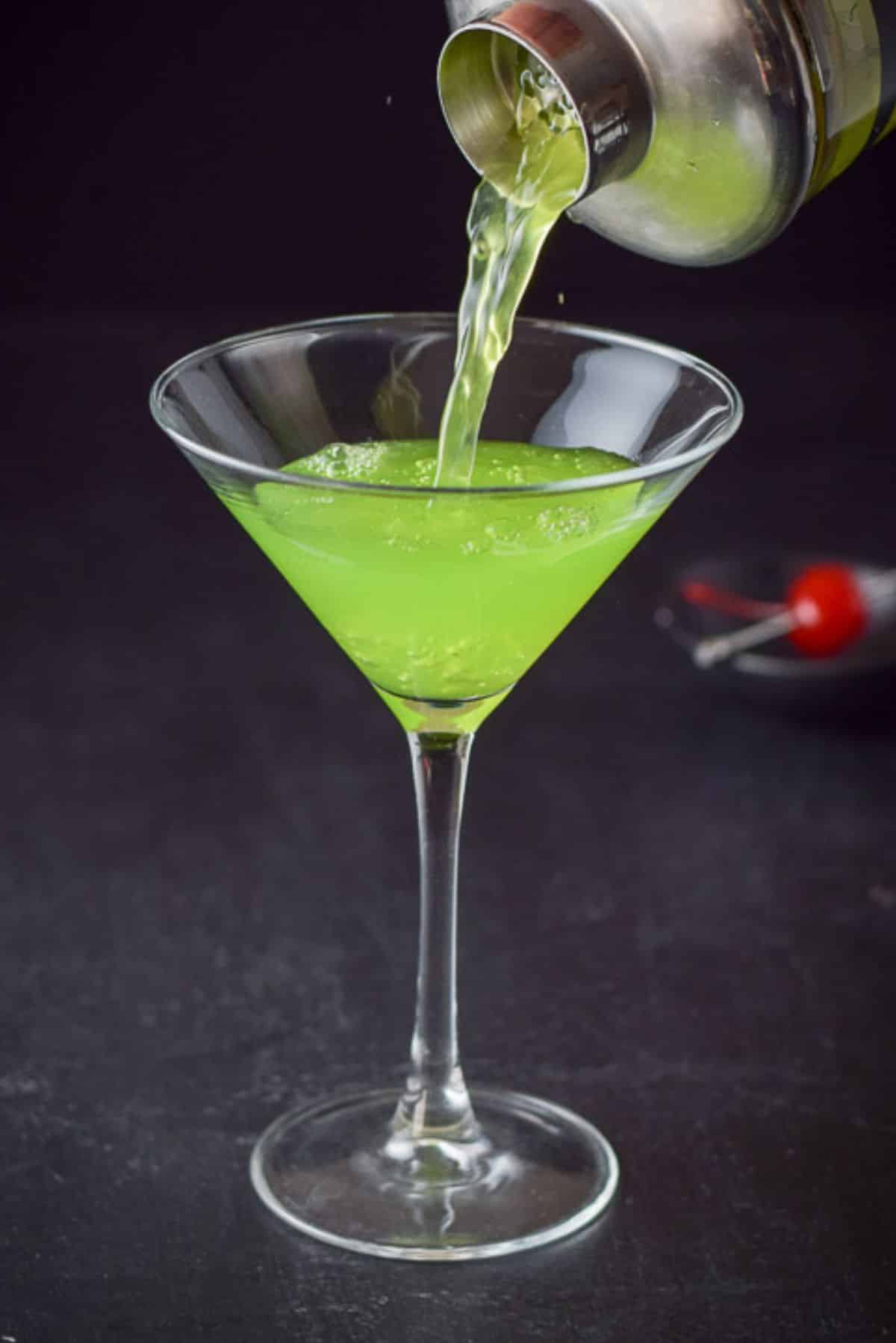 Green liquid coming out of a cocktail shaker and into the martini glass